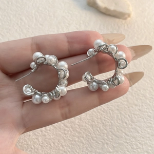 Silver C-shaped hoop earrings with embedded white pearls shown held in hand