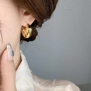 Vue de profil d'une femme portant de larges créoles dorées en forme de C au style épuré