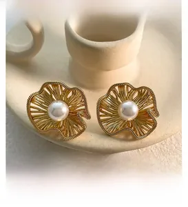 Macro shot of matte gold pleated flower earrings featuring a central white pearl detail