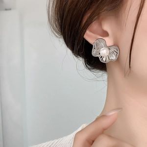 Close-up of matte silver flower stud earrings with a large white pearl on model