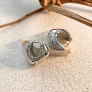 Vue macro de boucles d'oreilles créoles abstraites argentées sur socle en pierre