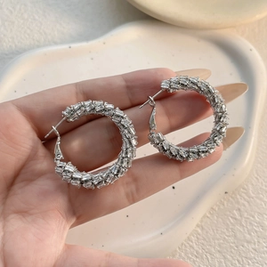 Macro detail of silver hoop earrings featuring baguette-cut zircon in a hand-held view