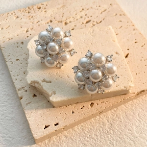 Macro shot of pearl and zircon flower stud earrings on natural beige stone texture