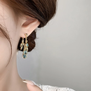 Close-up of golden tassel earrings with mint blue zircon pendants on a female model