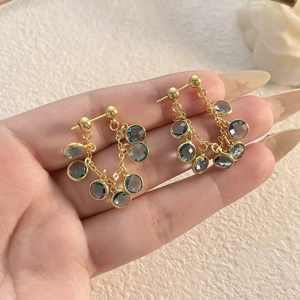 Elegant gold-plated hoop earrings with mint blue zircon tassels held in hand for scale