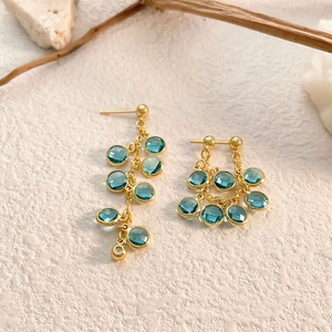 Detail of gold tassel earrings with mint blue zircon pendants on natural stone background