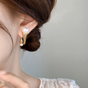 Detail of elegant gold curved pearl earrings worn on ear with white lace outfit