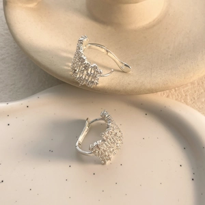 Close-up of geometric hollow silver earrings with pavé crystals on cream ceramic tray