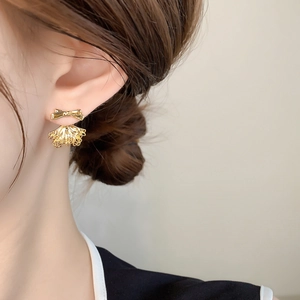 Close-up of golden bow stud earrings with delicate lace fan drops on model's ear