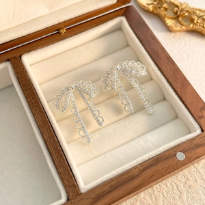 Detailed view of silver lace bow earrings with long tassels on a walnut jewelry box