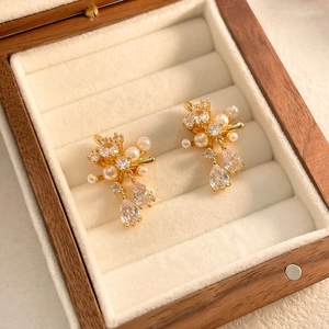 Detailed shot of gold floral earrings with cluster pearls and teardrop zircons on velvet