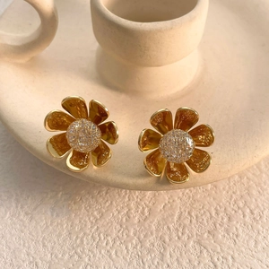 Detail of 3D golden sunflower stud earring with crystal core resting on ceramic cup