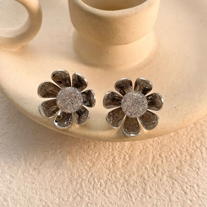 Macro detail of silver flower earrings with textured center on ceramic base