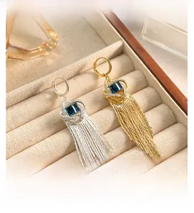 Détail macro de boucles d'oreilles à pompons longs avec pierres carrées bleu foncé et pavé