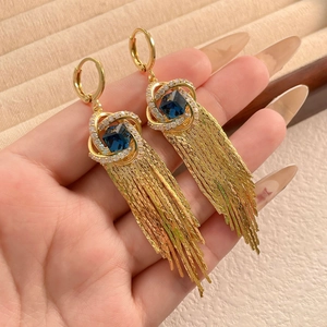 Boucles d'oreilles dorées à franges avec pierre bleue et zircons blancs tenues à la main