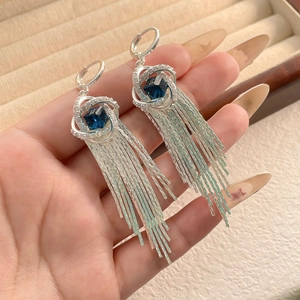 Détail de boucles d'oreilles pompons argentées avec zircons bleus et cristaux brillants