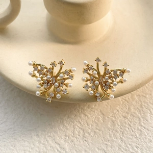 Close-up of gold butterfly stud earrings with sparkling white zircons and pearls