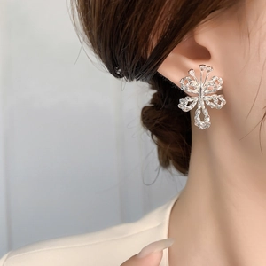 Detailed view of silver bow-shaped earring with crystals worn on a model's ear