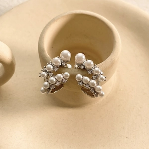 Dettaglio di orecchini a clip vintage con perle e zirconi su bordo di tazza beige