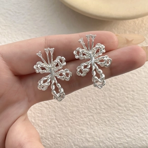 Silver bow knot earrings with twisted metal texture and zircon stones on a hand