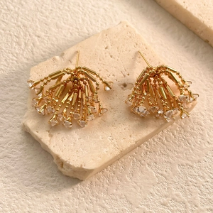 Close-up of golden tassel earrings with sparkling cubic zirconia on stone texture
