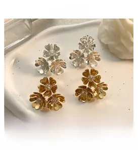 Macro shot of gold and silver three-petal flower stud earrings on a wavy white tray