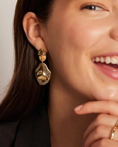 Detailed close-up of golden teardrop earrings with hammered lava texture on a model