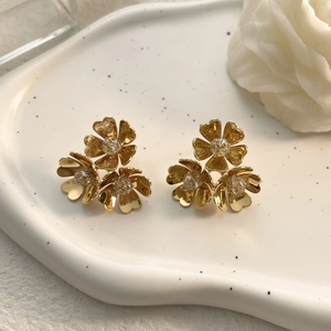 Detailed close-up of golden flower stud earrings with rhinestones on a ceramic tray
