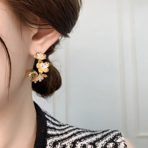 Macro view of golden floral earrings with crystal centers worn by a model