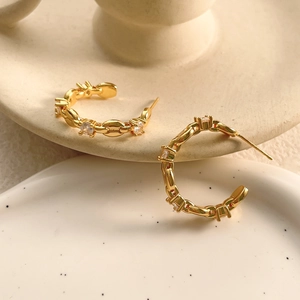 Detailansicht goldener C-Creolen mit Zirkonia-Steinen auf einer Keramikschale
