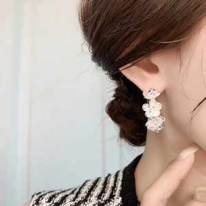 Close-up of silver triple-flower drop earrings with textured petals and inlaid crystals