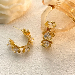 Detail of floral earrings featuring gold metal petals and crystal center on texture