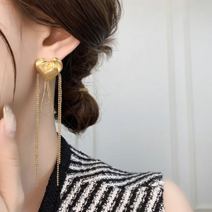 Detail of gold heart stud earrings with long beaded tassels worn by a female model