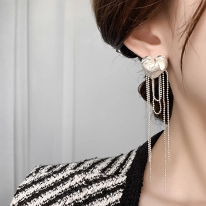 Detail of silver heart earrings with long beaded tassels on model with tweed jacket