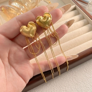 Close-up of gold plated heart earrings with long bead chain tassels held in hand
