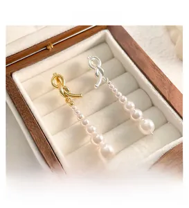 Gros plan de boucles d'oreilles nœud asymétriques avec perles blanches dégradées