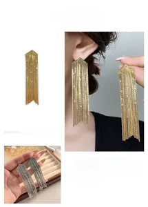 Détail de boucles d'oreilles à longs pompons avec flèche et strass dorés et argentés