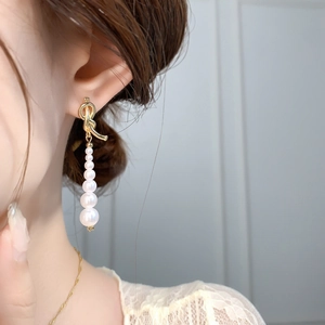 Détail de boucles d'oreilles nœud doré avec cinq perles blanches dégradées sur mannequin
