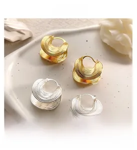 Detailed view of layered wavy textured metal hoop earrings in gold and silver finishes