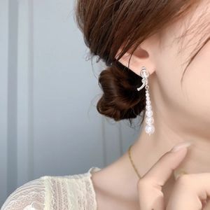 Détail de boucles d'oreilles perles avec nœuds argentés et cinq perles blanches