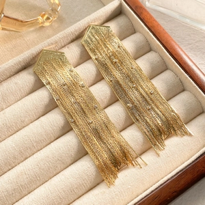 Vue détaillée de boucles d'oreilles dorées à pompons avec strass dans un écrin velours
