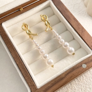 Détail de boucles d'oreilles nœud doré avec six perles dégradées sur support en velours