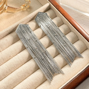 Détail de longues boucles d'oreilles à pompons argentés avec chaînes fines et strass
