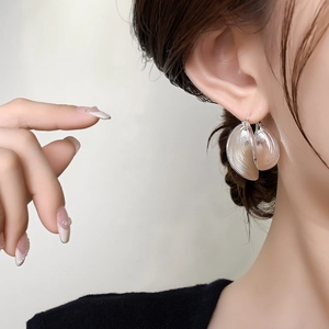 Close-up of silver metal hoop earrings with elegant vertical leaf texture on model
