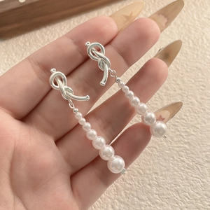 Boucles d'oreilles nœud argenté avec perles blanches dégradées sur fond chaleureux