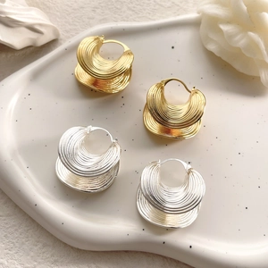 Detail of layered gold and silver hoop earrings with unique wavy textured leaf pattern