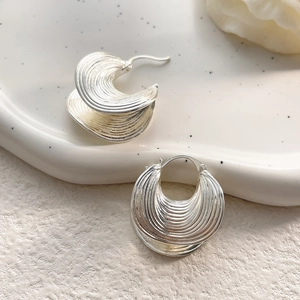 Macro view of silver vintage textured hoop earrings with artistic spiral leaf pattern