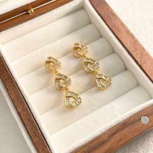Detailed view of triple triangle zircon drop earrings in gold on white velvet display