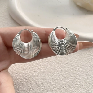 Silver hoop earrings with layered fan-shaped textures and metallic finish shown by hand