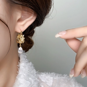 Close-up of gold hollow flower earrings with pear-cut crystal on a female model